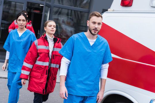 young male and female paramedics walking near ambulance