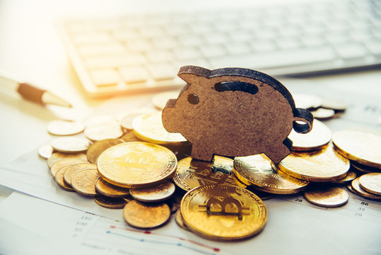 bitcoins are placed on the area with the sign of piggy bank overlaid on the area of the working table with a laptop. - The concept of saving money