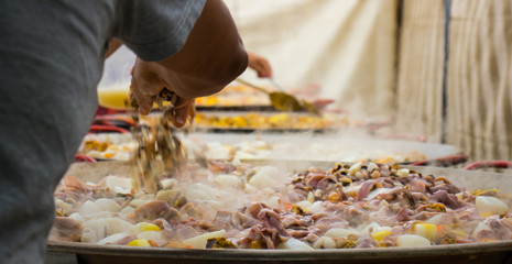 Adding seafood to huge frying pans.People are preparing a giant paella.