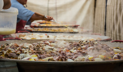 People are preparing a giant paella. Adding seafood to huge frying pans.