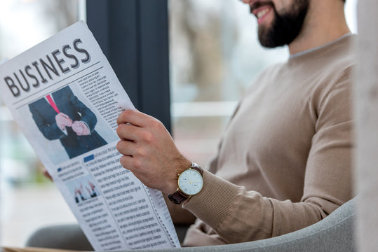 cropped image of smiling businessman sitting in cafe and reading newspaper
