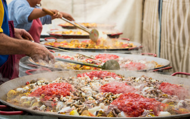 People mix in pans paella with tomato sauce.