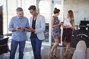 Male business colleagues using mobile phones at creative office