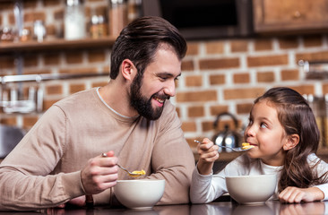 smiling father and daughter eating breakfast and looking at each other