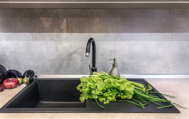 Washed vegetables and greens lie on a clean table top in a modern kitchen