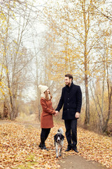 Couple walking with dog in the Park and hugging. Autumn walk men and women with a dog. Romance and love on an autumn landscape