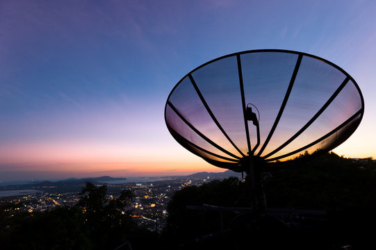 Satellite dish at sunset.Satellite television dish on the hill over city bay at twilight  sunset.