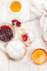 Tea time with festive sufganiyot donuts filled with jelly and covered with sugar powder. White wooden background, bright lighting. Vertical composition.
