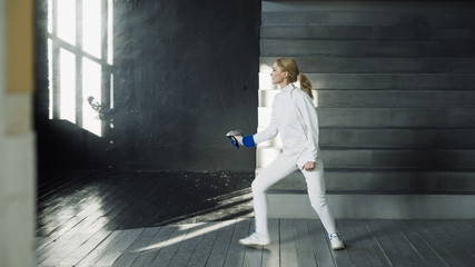 Young concentrated fencer woman practice fencing exercises and training for Olympic games competition in studio indoors