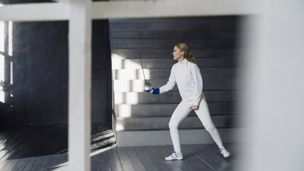 Fototapeta na wymiar Young concentrated fencer woman practice fencing exercises and training for Olympic games competition in studio indoors