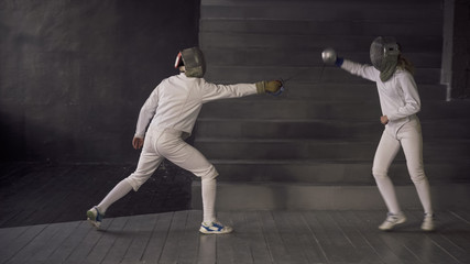 Two fencers man and woman have fencing match indoors