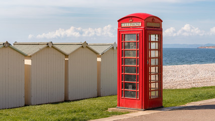Telephone Booth behind some beach huts at Budleigh Salterton beach, Jurassic Coast, Devon, England, UK