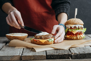 cropped view of girl in apron making tasty homemade cheeseburgers on baking paper on wooden tabletop