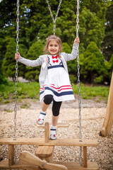 Cute little girl on a swing. Smiling child playing outdoors in summer.