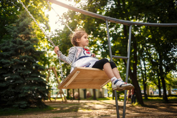 Cute little girl on a swing. Smiling child playing outdoors in summer.
