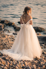 Fototapeta na wymiar Romantic beautiful bride in white dress posing on sea and mountains in background