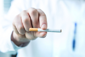 Doctor holding one cigarette between fingers. Quit smoking concept.