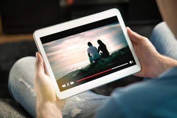 Online movie stream with mobile device. Man watching film on tablet with imaginary video player...