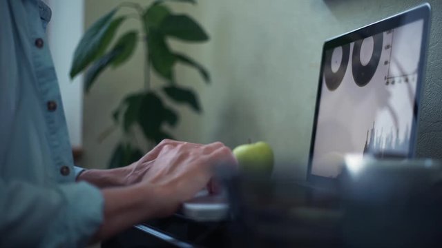 Casual dressed young man using laptop making notes in notepad at home