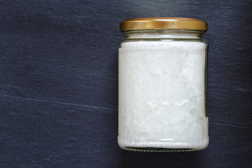 Glass jar with fresh coconut oil on slate