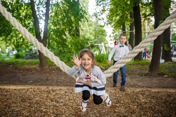 Happy little girl and boy on a rope swing. Children playing outdoors in summer.