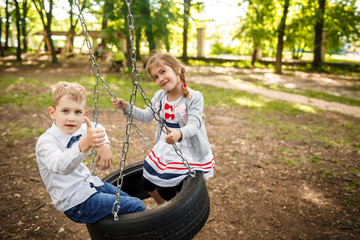 Boy and girl on a tire swing. Children playing outdoors in summer.