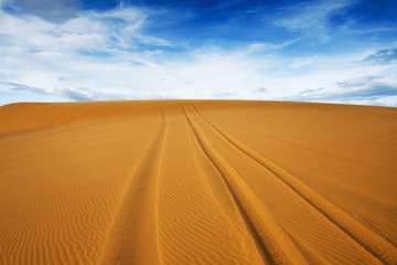Fototapeta na wymiar Bright yellow sand empties against the blue sky with clouds. The arid region of the planet