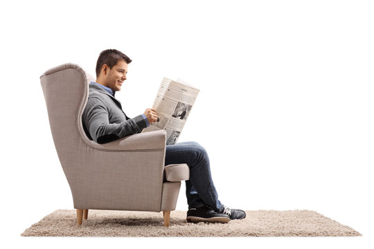 Young guy seated in an armchair reading a newspaper