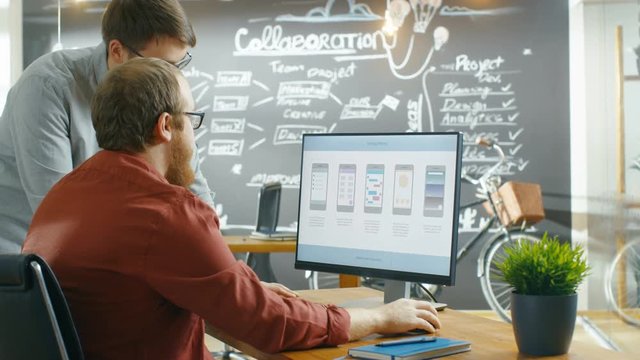 Two Male Mobile Game Application Developers Talk while Working on a Personal Computer, Designing Wireframe. Shot on RED EPIC-W 8K Helium Cinema Camera.