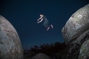 From below view of sportive man jumping from rock to rock doing parkour in dark night. 