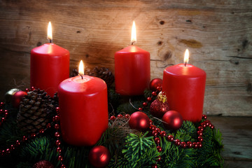 Advent wreath from fresh fir tree branches with four red burning candles and christmas decoration on rustic  wood