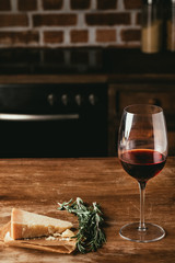 glass of red wine, Parmesan cheese and fresh rosemary on wooden tabletop in kitchen