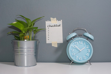 Alarm clock and a piece of note stick on the wall with text CHECKLIST.