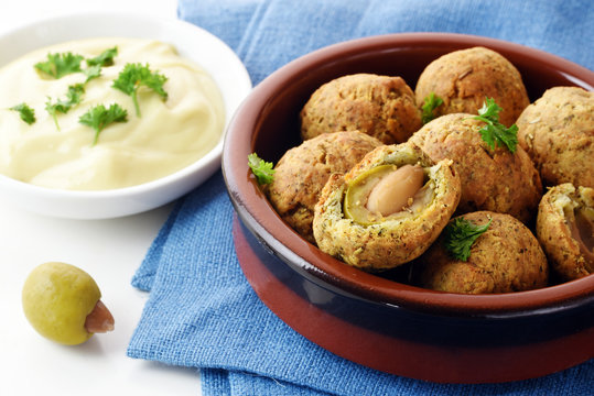 Green olives baked in parmesan dough with a creamy garlic dip, finger food for the party buffet, spanish tapas appetizer, brown ceramic bowl on a blue naplin on a white table