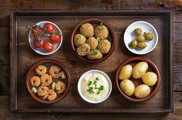 Rucksack Spanish tapas such as baked olives, prawn shrimps, potatoes, tomato and garlic dip, party  appetizers on a rustic wooden tray, flat top view from above © Maren Winter