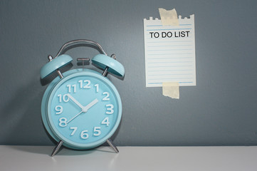 Blue Alarm clock and a note paper stick on the wall with text To Do List.