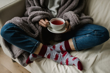 Feet in woollen socks. Woman is relaxing with a cup of hot drink and warming up her feet in woollen socks. - 182966927