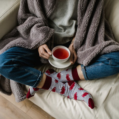 Feet in woollen socks. Woman is relaxing with a cup of hot drink and warming up her feet in woollen socks. - 182967113
