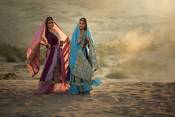 Two happy women wearing Iran or Arabian traditional dress stand by the sand.