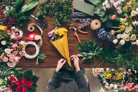 cropped image of florist tying ribbon on bouquet at flower shop