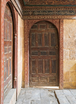 Two wooden aged ornate vaulted perpendicular doors on stone bricks walls, Medieval Cairo, Egypt