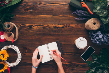 cropped image of female florist writing down something to working notebook