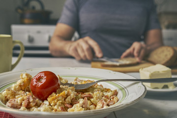 Freshly made omelette with sausages  in a plate on the foreground and a man smearing a butter on bread on blurred background    