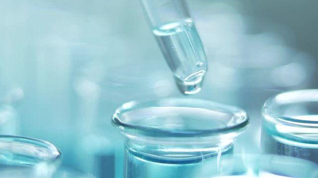 In a laboratory, a scientist with a pipette analyzes a blue liquid to extract the DNA and molecules in the test tubes. Doctor working with liquid.