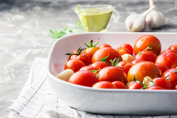 Fresh cherry tomatoes with thyme, olive oil, rosemary garlic cloves in baking dish. Selective focus, close up. 