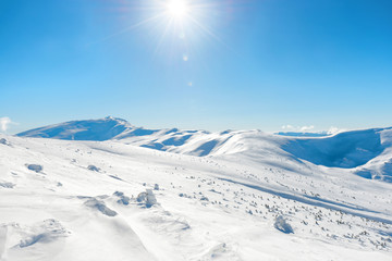 Obraz premium White winter mountains with snow and bright shining sun and sunrays