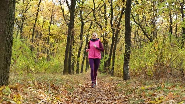 Slow motion Running - woman runner jogging on autumn forest path. Fit female sport fitness model athlete trail running training. Runner girl in sportswear running in park exercising outdoors.