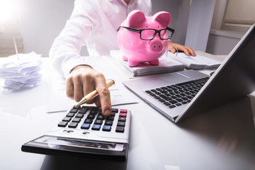 Businessman Calculating Tax Using Calculator With Piggybank