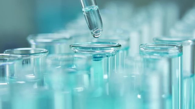 In a laboratory, a scientist with a pipette analyzes a blue liquid to extract the DNA and molecules in the test tubes. Doctor working with liquid.
