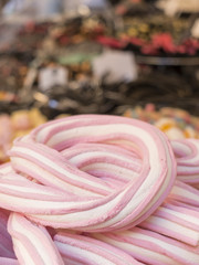 Fototapeta premium braid of pink and white marshmallow in the foreground. Variety of colorful candies on the background
